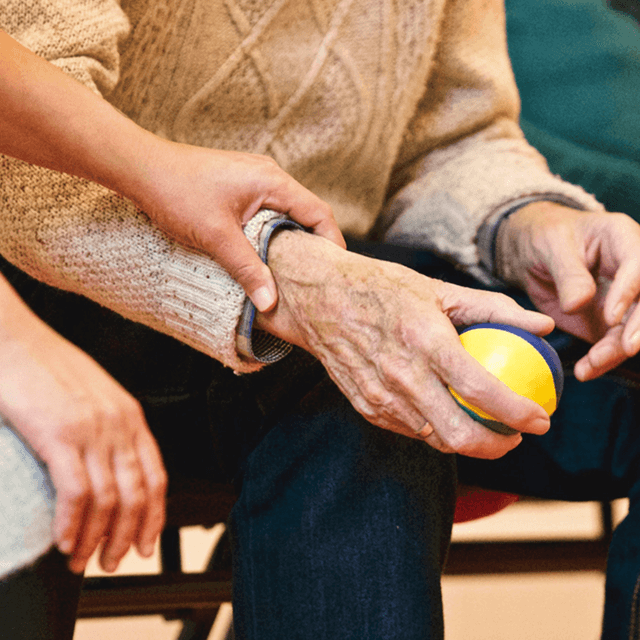 senior citizen gripping ball with assistance from nurse's hand